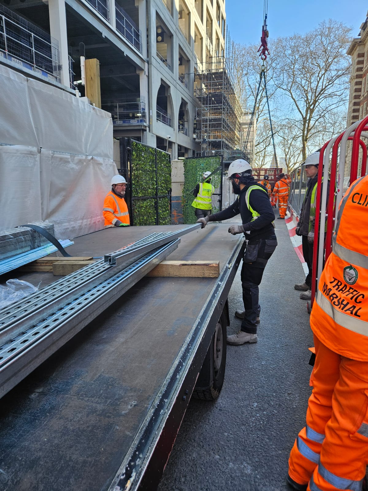 Flatbed offloading steel at a central London construction site with traffic marshal